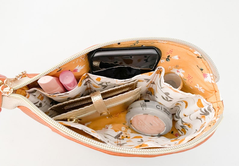 May include: An orange zippered pouch with a floral print lining. The pouch is open and contains a phone, wallet, makeup, and other small items.
