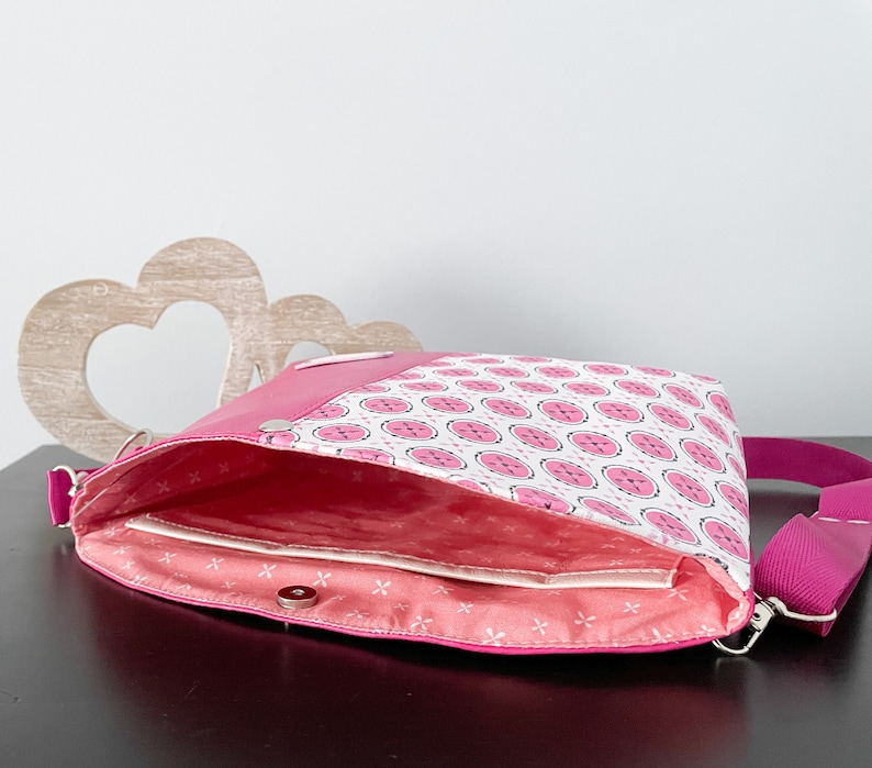 May include: A pink and white patterned crossbody bag with a pink strap. The bag is open and the inside is lined with a pink fabric.
