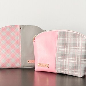 May include: Two pink and gray patterned cosmetic bags with gold zippers and a gold nameplate. The bag on the left has a pink and white plaid pattern and a gray fabric panel. The bag on the right has a solid pink panel and a gray and white plaid pattern.