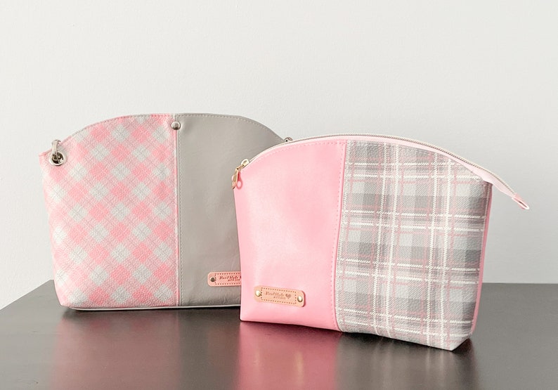 May include: Two pink and gray patterned cosmetic bags with gold zippers and a gold nameplate. The bag on the left has a pink and white plaid pattern and a gray fabric panel. The bag on the right has a solid pink panel and a gray and white plaid pattern.