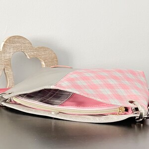May include: A pink and gray checkered fabric handbag with a zipper closure and a silver clasp. The bag has a gray leather strap.