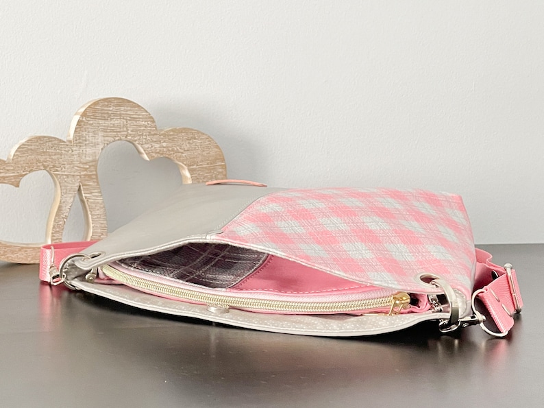 May include: A pink and gray checkered fabric handbag with a zipper closure and a silver clasp. The bag has a gray leather strap.