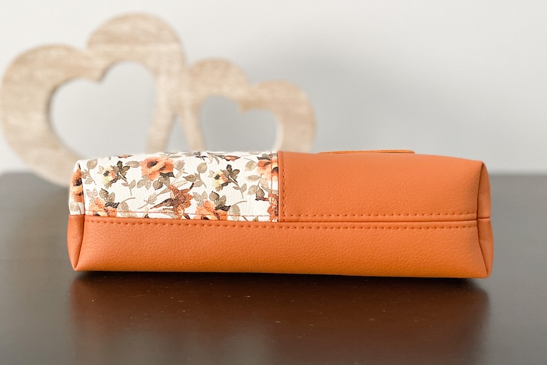 May include: A small orange and white floral patterned clutch purse with a zipper closure.