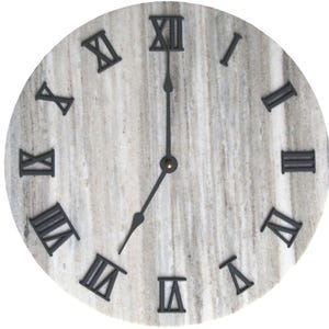 May include: Round wall clock with a light gray marble-like face and black Roman numerals. The clock hands are black, and the time displayed is approximately 7:00. A decorative piece for home decor.