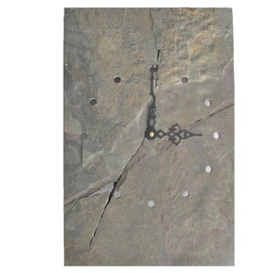 May include: A square slate clock with black hands and a gold center. The clock face is made of natural slate with a gray and brown color scheme. The slate is broken into several pieces, giving the clock a rustic look.