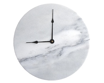 May include: Round marble clock with black hands and a gold center. The clock face is white with gray veining. The hands point to approximately 8:40.