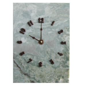 May include: A rectangular wall clock with a green and white marble face. The clock features bronze-colored numerals and hands, indicating the time is approximately 9:59. The clock's face has a natural, veined pattern.