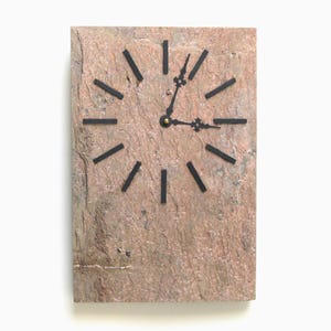 May include: A rectangular wall clock with a textured, reddish-brown stone face. Black hands and hour markers contrast against the stone. The clock's design is simple and modern, suitable for various interior styles.