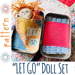 Pode incluir: Uma pequena boneca com cabelo ruivo está enfiada em uma bolsa de tecido com as palavras "LET GO" nela. A boneca está dentro de uma pequena lata com um tecido listrado azul e branco e um cartão rosa com o texto "Tell me your worries, Fears and frets. I'll carry them tonight, you'll have no regrets. It's time to LET GO, Snooze and rest. You've done all you can And gave it your best. Sweet Dreams".