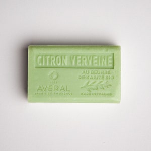 May include: A green bar of soap with the text "CITRON VERVEINE" in white lettering. The soap also has the text "AU BEURRE DE KARITÉ BIO" and "MADE IN FRANCE" in white lettering. The soap is labeled "AVERAL SAVON DE PROVENCE" and has a small circle with the number "1985" inside.