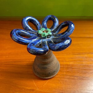 May include: A blue ceramic flower with a green center. The flower is on a brown wooden surface.