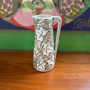 May include: White ceramic pitcher with a brown ivy design. The pitcher has a tall, slender shape and a handle on the side.