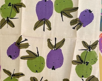 May include: A white linen tea towel with a repeating pattern of green, purple, and blue stylized apples. The towel is signed "Usma" in the bottom right corner.