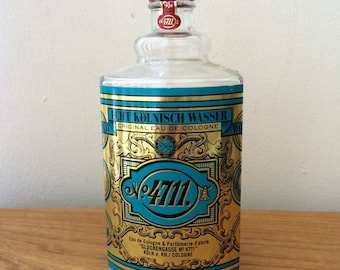 May include: A clear glass bottle of 4711 Original Eau de Cologne. The bottle has a gold label with the text "4711. Eau de Cologne & Parfümerie-Fabrik "GLOCKENGASSE NO 4711" KOLN a. RH./COLOGNE" in black and gold lettering.