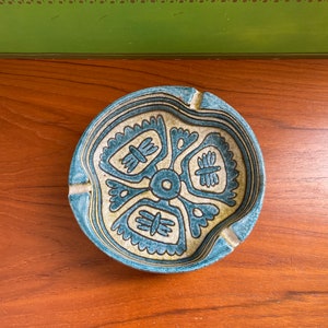 May include: A blue and white ceramic ashtray with a geometric design. The ashtray has a wavy edge and a center hole.