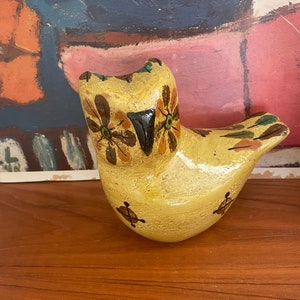 May include: A hand-painted ceramic owl figurine with brown and green accents. The owl has a yellow body with brown and green floral designs and a black beak.