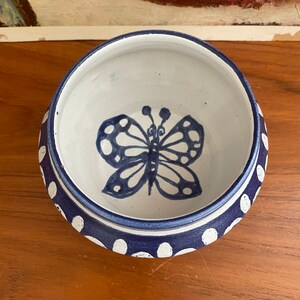 May include: A white ceramic bowl with a blue butterfly design and white polka dots around the rim.