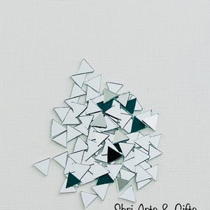 May include: A pile of small, silver, triangular mirror tiles. The tiles are scattered on a white surface. The text "Shri Arts & Gifts" is visible at the bottom of the image.