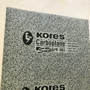 May include: A sheet of grey Kores Carboplane Super 503 tracing paper. The paper is textured and has a black and white speckled pattern. The text on the sheet reads "Kores Carboplane Super 503 NON CURLING NON SMUDGING LIGHT FAST LONG LASTING".