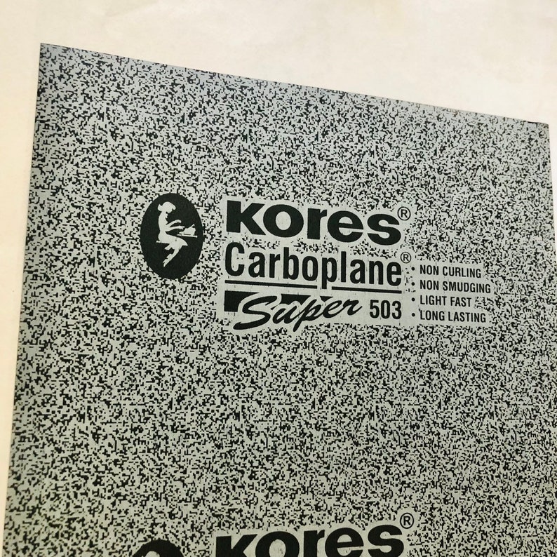 May include: A sheet of grey Kores Carboplane Super 503 tracing paper. The paper is textured and has a black and white speckled pattern. The text on the sheet reads "Kores Carboplane Super 503 NON CURLING NON SMUDGING LIGHT FAST LONG LASTING".