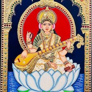 Puede incluir: Una pintura vibrante de una deidad sentada sobre una flor de loto blanca, tocando un instrumento de cuerda. La figura está adornada con joyas de oro y una corona, sobre un fondo rojo y un fondo azul oscuro con detalles dorados ornamentados.
