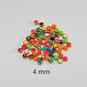 May include: A collection of small, colorful, round embellishments with a gold-colored border. The gems are in various colors, including pink, green, blue, and yellow. The text "4 mm" is displayed below the embellishments, indicating their size.