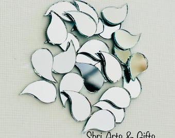 May include: A collection of silver teardrop-shaped mirror tiles. The tiles are arranged in a loose cluster, with some overlapping. The tiles are all the same size and shape, and they have a smooth, reflective surface. The tiles are perfect for adding a touch of sparkle and glamour to any craft project.