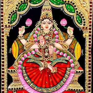 Puede incluir: Una pintura tradicional india que representa a una deidad, probablemente Lakshmi, la diosa de la riqueza y la prosperidad. Está sentada en un trono, adornada con joyas de oro y flores, y tiene cuatro brazos. La pintura está realizada en un estilo vibrante con acentos dorados y un fondo negro.