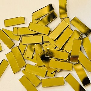 May include: A pile of gold-colored rectangular mirror tiles. The tiles are scattered on a white surface.