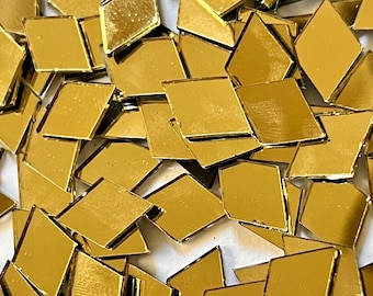 May include: A pile of gold-colored diamond-shaped mirror tiles. The tiles are scattered on a white surface.