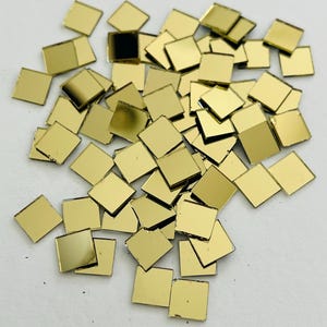 May include: A pile of small, square, gold-colored mirror tiles.