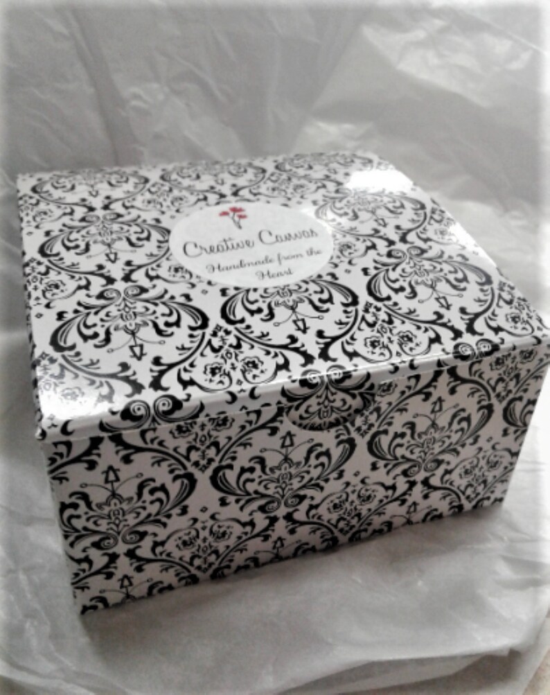 May include: A black and white damask patterned box with a white label that says "Creative Canvas Handmade from the Heart".