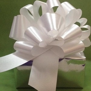 K&ouml;nnte beinhalten: Eine silberne Geschenkbox mit einer gro&szlig;en wei&szlig;en Schleife aus Satin. Die Schleife ist mit einem langen wei&szlig;en Band gebunden.