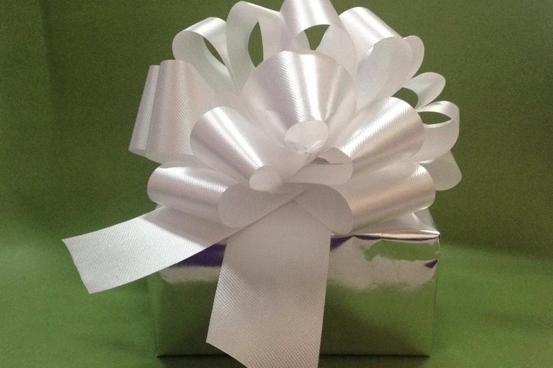 K&ouml;nnte beinhalten: Eine silberne Geschenkbox mit einer gro&szlig;en wei&szlig;en Schleife aus Satin. Die Schleife ist mit einem langen wei&szlig;en Band gebunden.