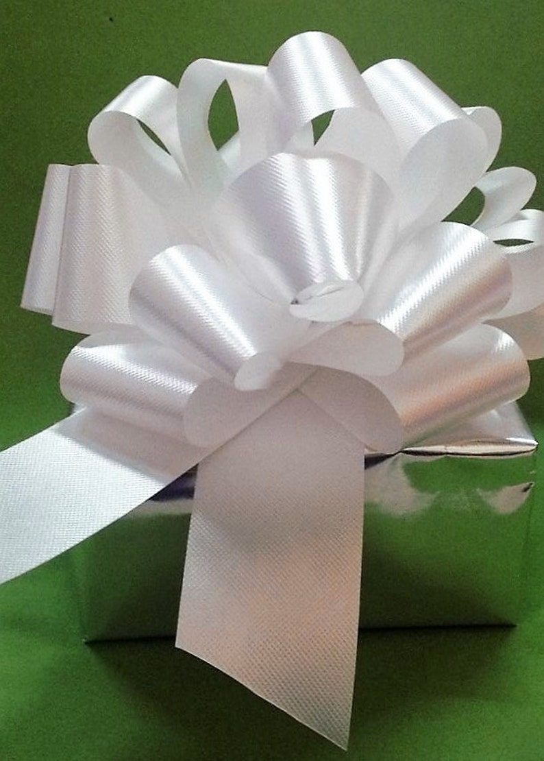 K&ouml;nnte beinhalten: Eine wei&szlig;e Satin Schleife, die auf einem silbernen Geschenkbox gebunden ist. Die Schleife ist gro&szlig; und flauschig, mit mehreren Schleifen und B&auml;ndern. Die Geschenkbox ist in silbernes Papier eingewickelt und hat einen gr&uuml;nen Hintergrund.