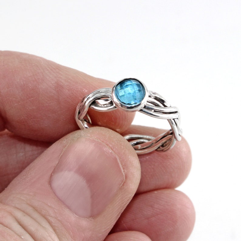May include: A silver ring with a braided band and a blue gemstone in the centre.