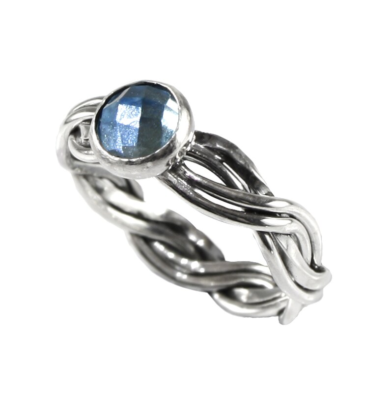 May include: A silver ring with a braided band and a blue gemstone in the centre.