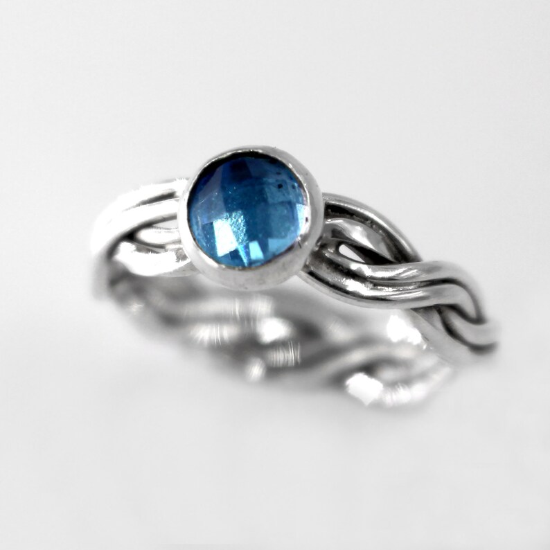 May include: A silver ring with a braided band and a blue gemstone.