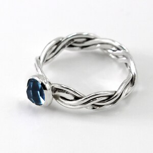 May include: A silver ring with a braided band and a blue gemstone.
