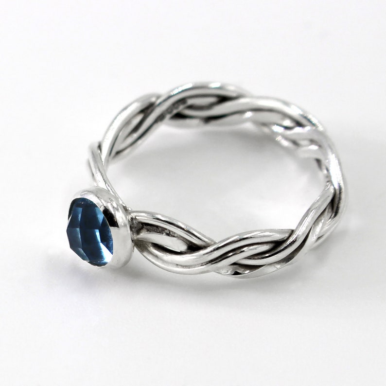 May include: A silver ring with a braided band and a blue gemstone.