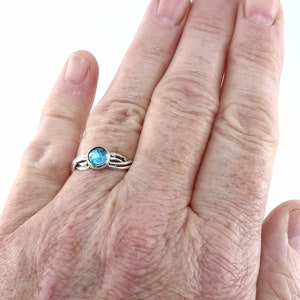 May include: A silver ring with a blue gemstone set in the centre. The ring has a twisted band design.