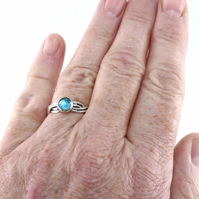 May include: A silver ring with a blue gemstone set in the centre. The ring has a twisted band design.