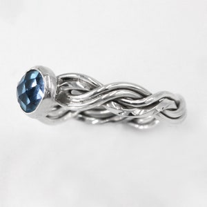 May include: A silver ring with a braided band and a blue gemstone set in the centre.