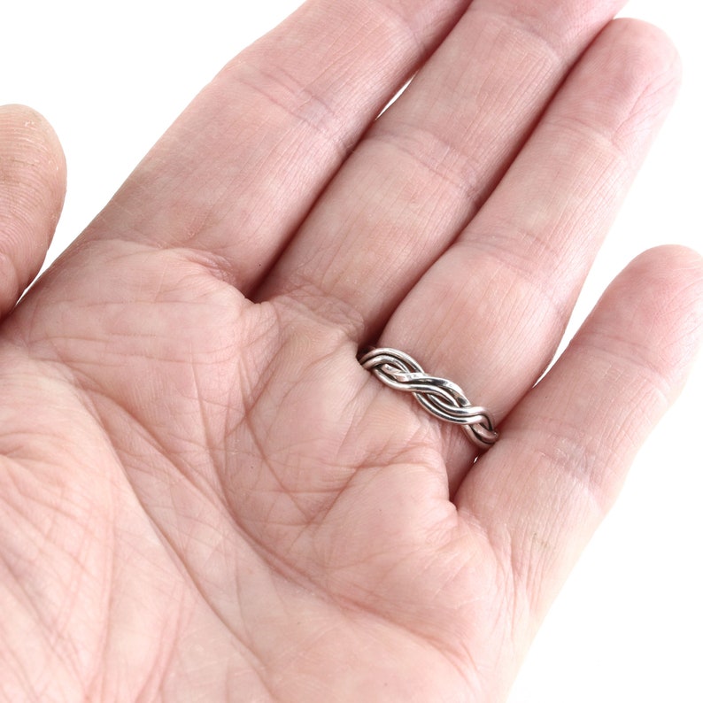 May include: A silver braided ring worn on a hand. The ring is made of three strands of silver wire that are twisted together.