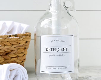 May include: A clear glass bottle with a white pump dispenser filled with liquid detergent. The bottle has a black and white label that reads "Hand Poured - Detergent - Signature Collection - Premium Quality".