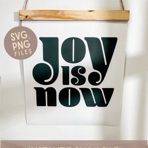May include: A digital download of a printable wall art design featuring the text "Joy is now" in a bold, stylized font. The design is in black and green on a white background.