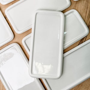 May include: A set of six white rectangular ceramic serving trays. The trays are stacked on top of each other, with the top tray slightly offset from the others.