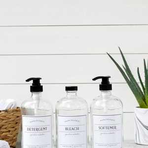 May include: Three clear glass bottles with black pump tops and labels. The labels read "HAND POURED", "DETERGENT", "BLEACH", "SOFTENER", "signature collection", and "PREMIUM QUALITY".