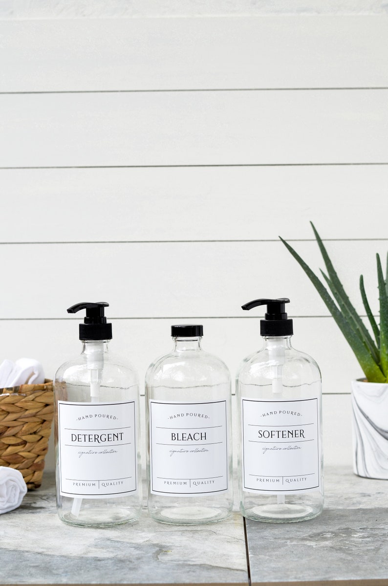May include: Three clear glass bottles with black pump tops and labels. The labels read "HAND POURED", "DETERGENT", "BLEACH", "SOFTENER", "signature collection", and "PREMIUM QUALITY".
