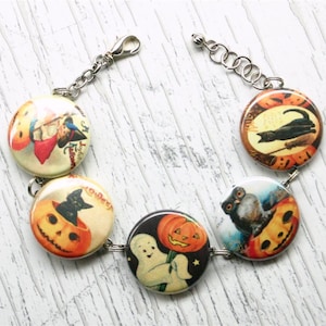 May include: A Halloween themed bracelet with five round buttons featuring vintage images of pumpkins, cats, owls, and a ghost. The buttons are connected by a silver chain.